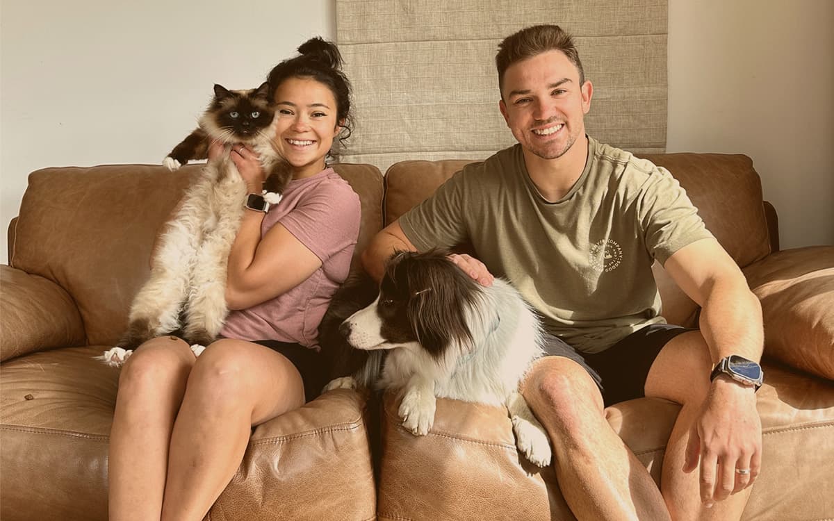 Maira and Miller sitting on the couch with a cat and a dog